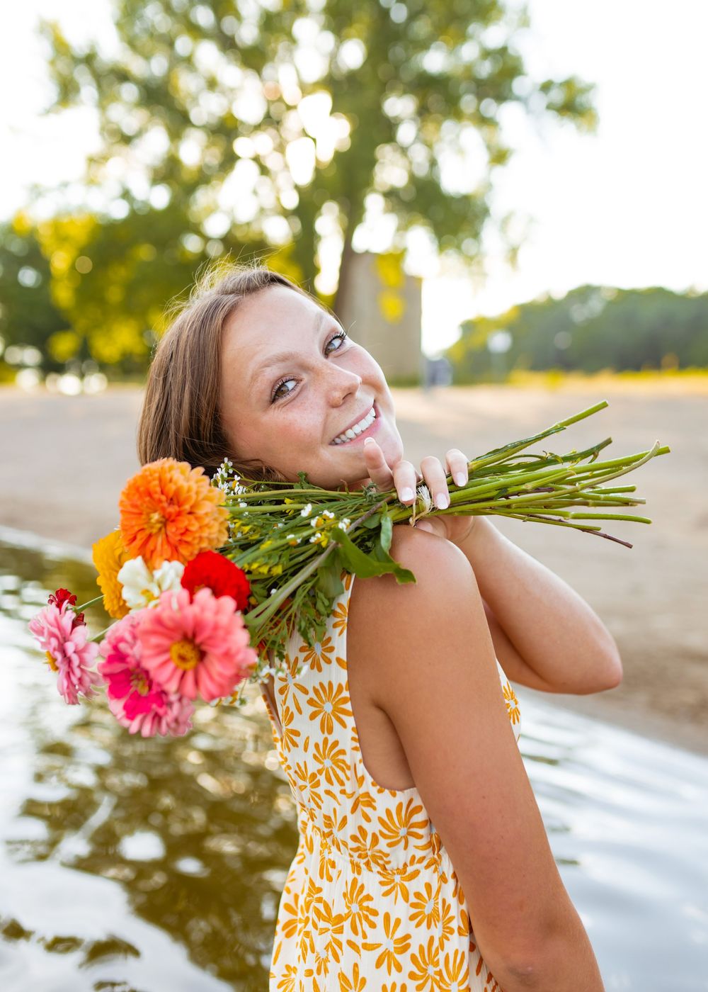 Someone in a yellow floral dress holds a cheerful bouquet of orange and pink gerbera daisies on a sunny summer day.