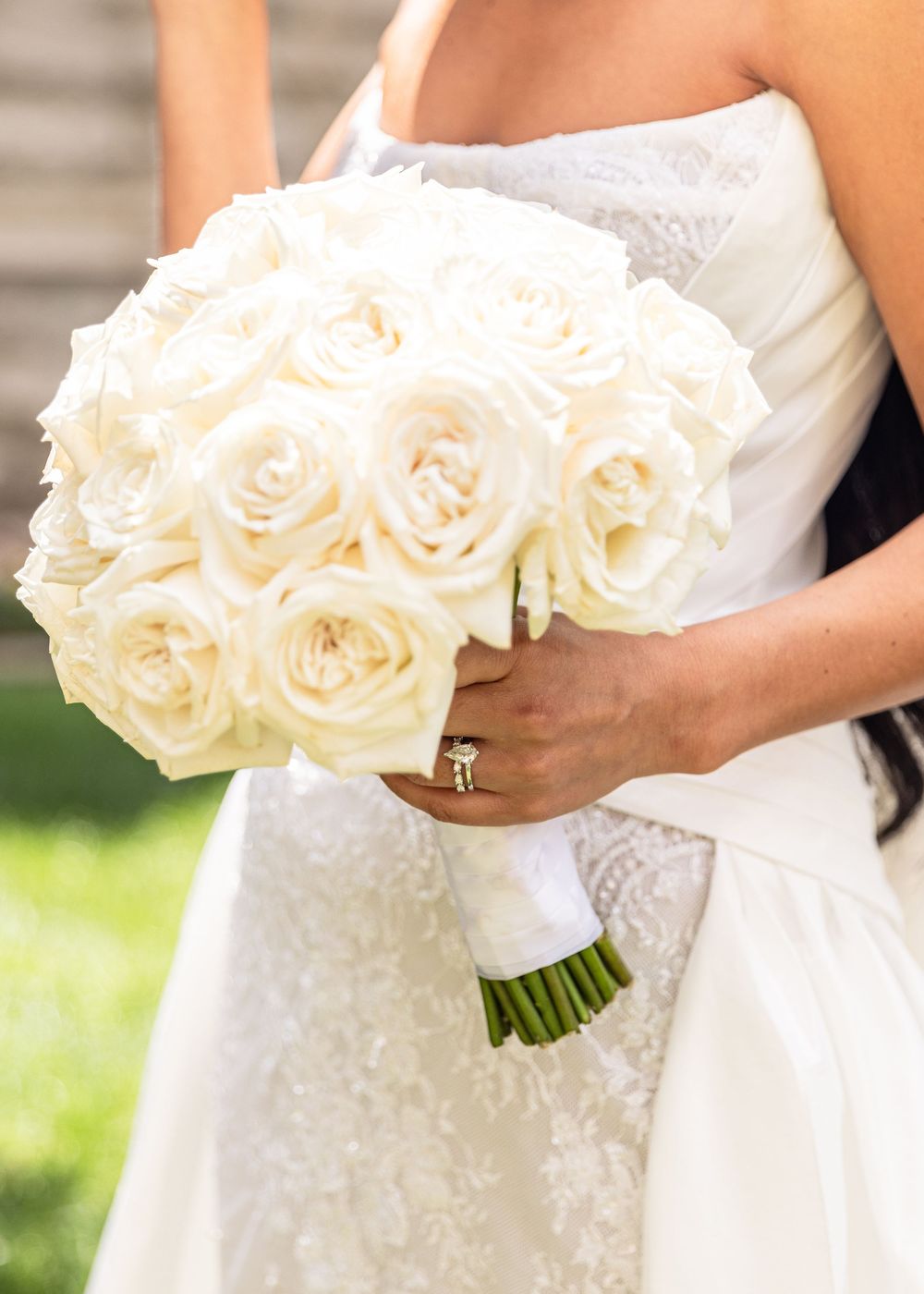 A wedding bouquet of elegant white roses is held against a white dress with delicate beading details.