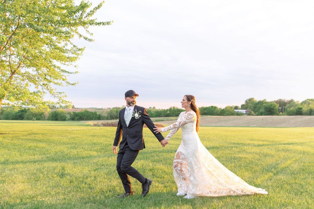 A couple in wedding attire walks hand in hand through a sunlit yellow meadow on a spring afternoon.