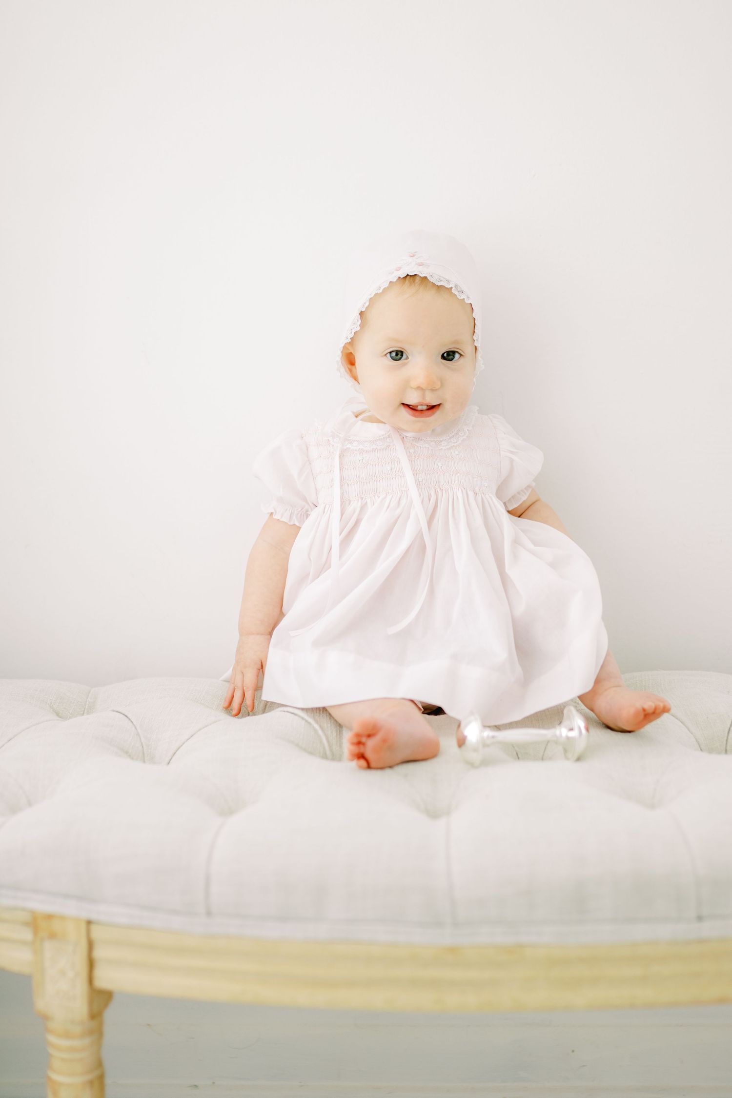 A small child in a light blue vintage-style bubble romper with lace trim and white bow hairpiece sits smiling.