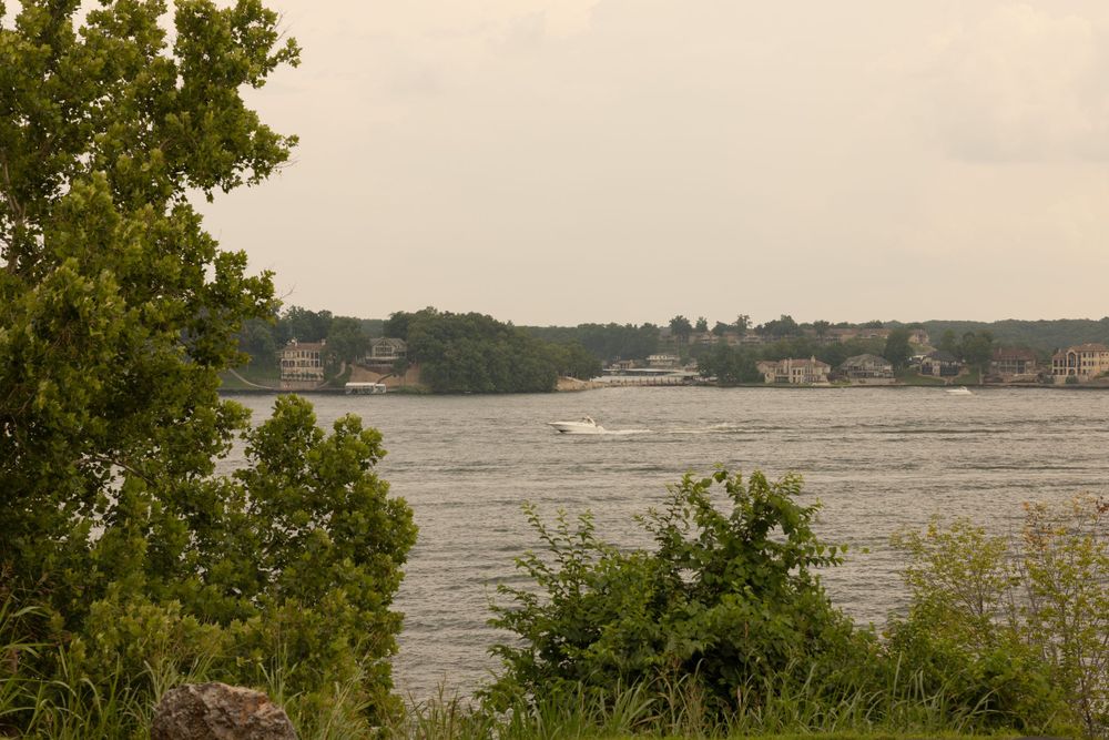 A scenic lake view through trees with boats visible in the distance on a cloudy day.