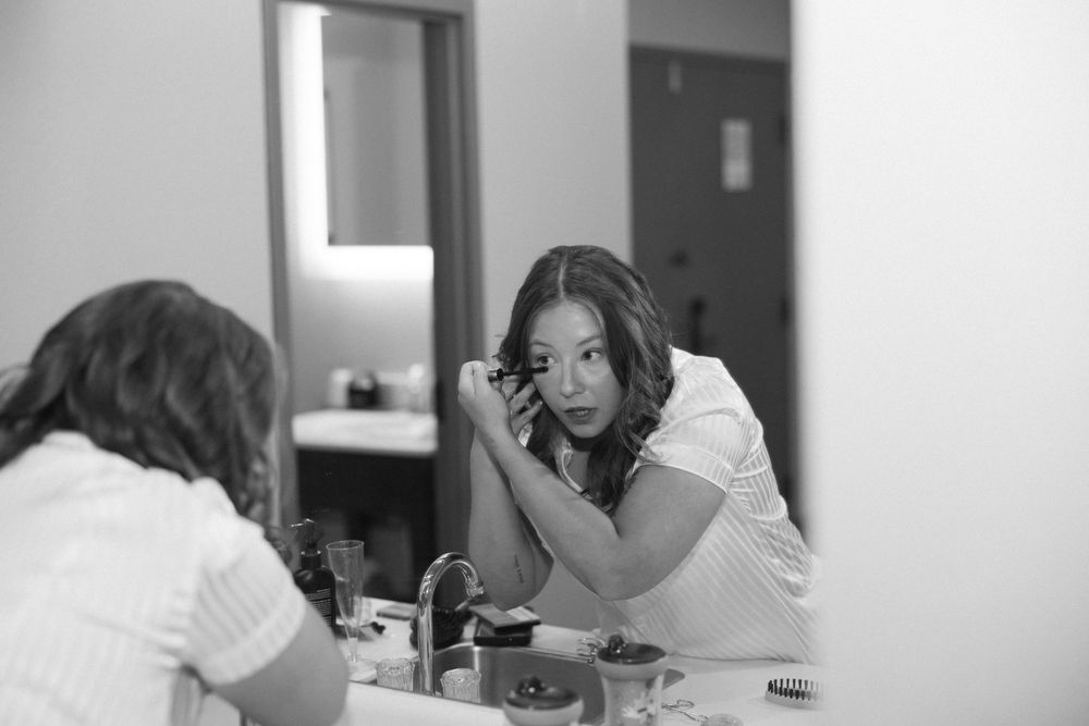 A black and white image of someone applying makeup in a bathroom mirror.