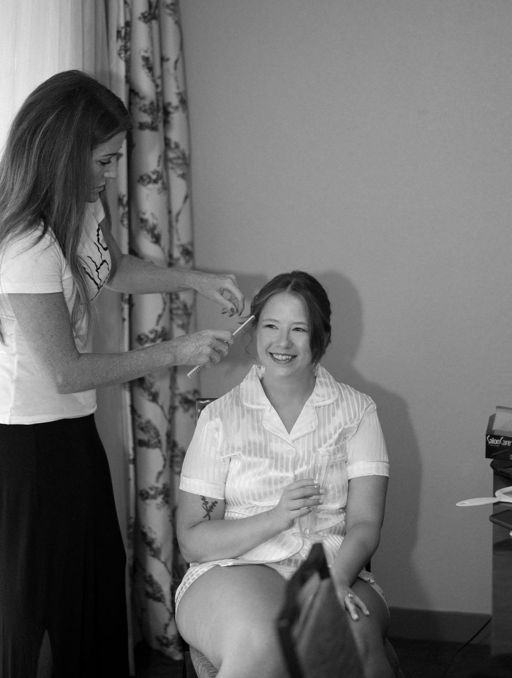 A candid moment during hair and makeup preparations in a bright room.
