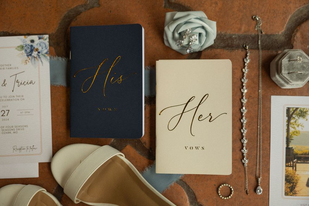His and her wedding vow books with elegant calligraphy displayed with rings and bridal accessories on a rustic surface.