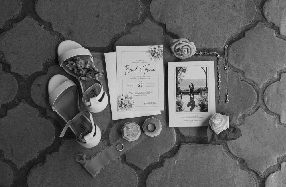 Black and white flatlay of wedding details including shoes, vow book and photograph on tile pattern.