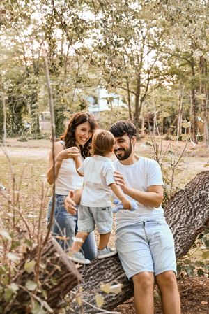 A happy young family with a toddler enjoying a sunny day outdoors near a fallen tree in a park.