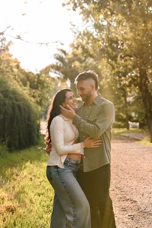 Couple embracing and smiling at each other on a sunny tree-lined path in golden hour light.