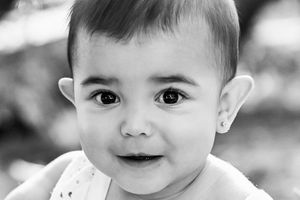 Black and white portrait of an adorable baby with big dark eyes and small ear stud, looking at camera.