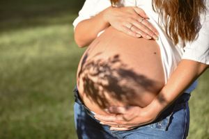 Close-up of pregnant belly with tree shadows casting beautiful patterns in natural sunlight.