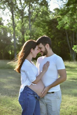 Romantic outdoor couple photoshoot in white outfits against sunlit forest background.