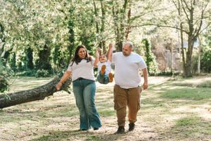 Family holding hands while walking together on wooded trail.