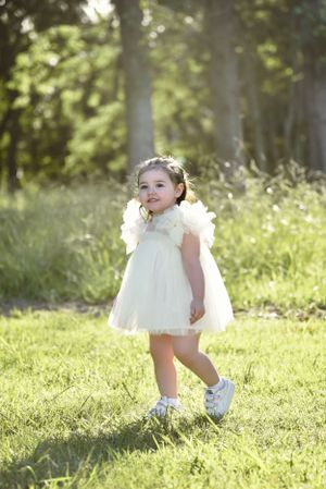 Delicate white dress contrasts beautifully with lush green grass in a sunlit outdoor portrait.