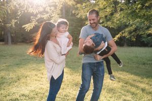 Family photo session in a sunlit park shows playful interactions and movement.
