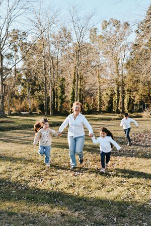 Sun-drenched autumn scene with people running and playing together in a grassy field surrounded by bare trees.
