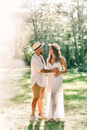 Sun-drenched maternity photo of couple in straw hats outdoors.