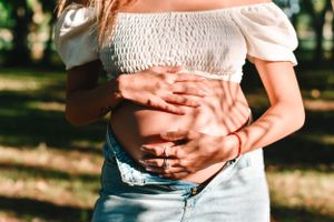 Close-up of hands cradling pregnant belly in casual summer outfit.