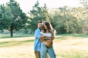 Outdoor couple session in a sun-drenched field with autumn trees in the background.