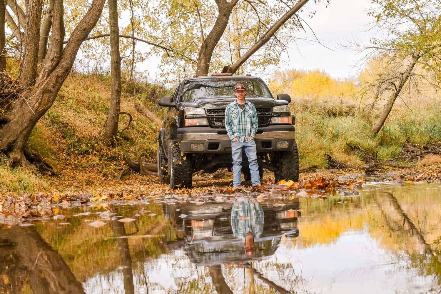A black pickup truck parked by a reflective pond during fall with autumn foliage and trees in the background.