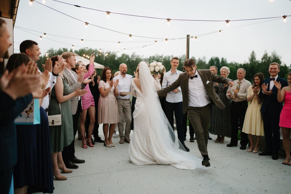 Wedding celebration with guests gathered outdoors under string lights during sunset.