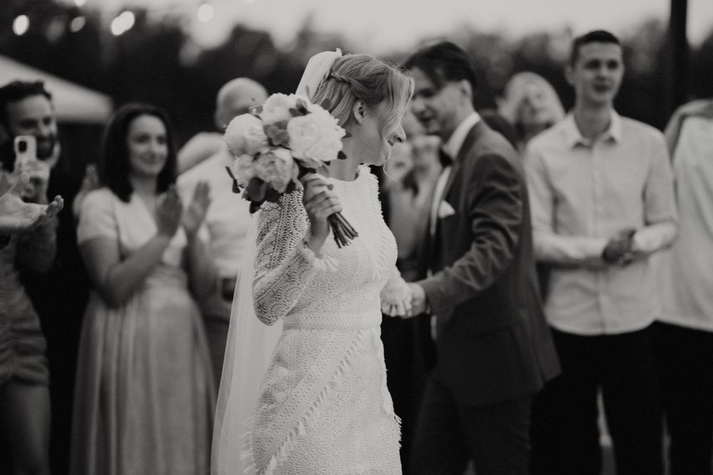 Black and white wedding photo of celebration with guests clapping outdoors.