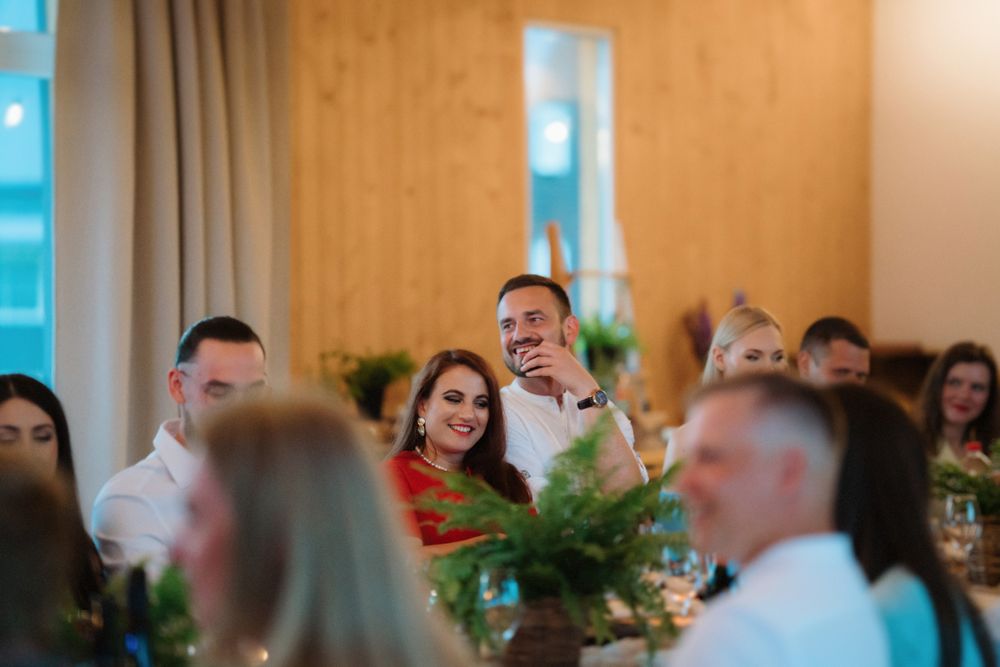 Wedding reception scene with guests seated at tables decorated with greenery and candles.