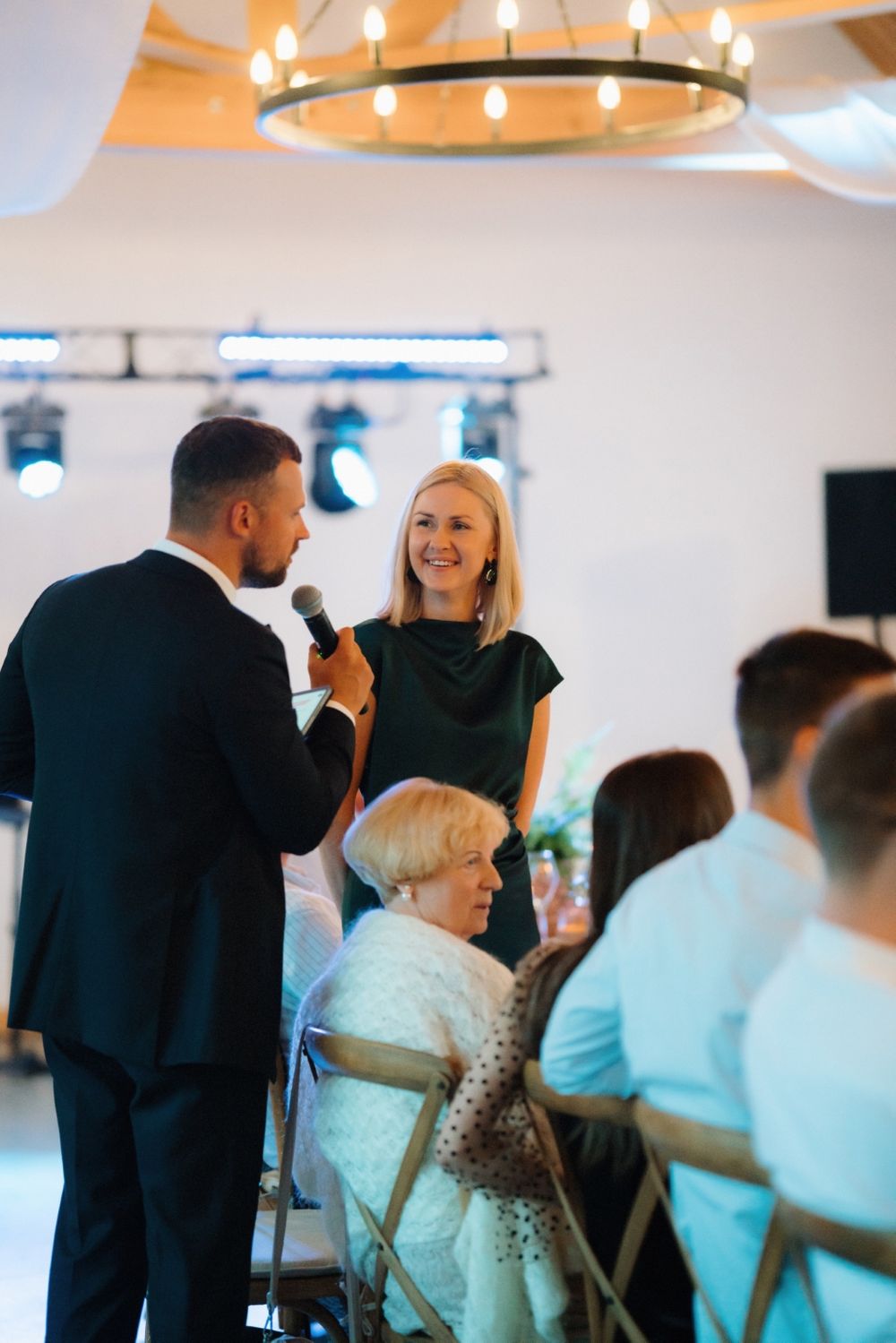 Wedding reception moment captured under circular chandelier in modern white venue.