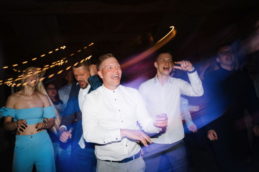 Party guests dancing under blue and purple lighting with string lights overhead.
