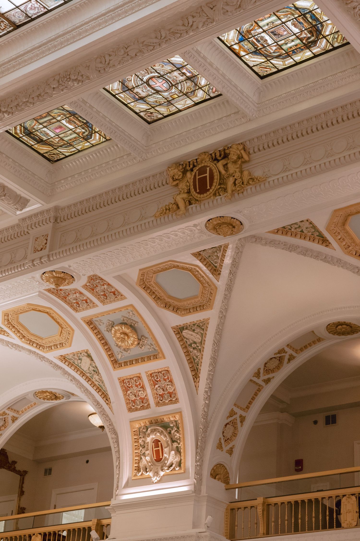 Ornate architectural details show stained glass skylights and gilded moldings in a classical interior ceiling design.