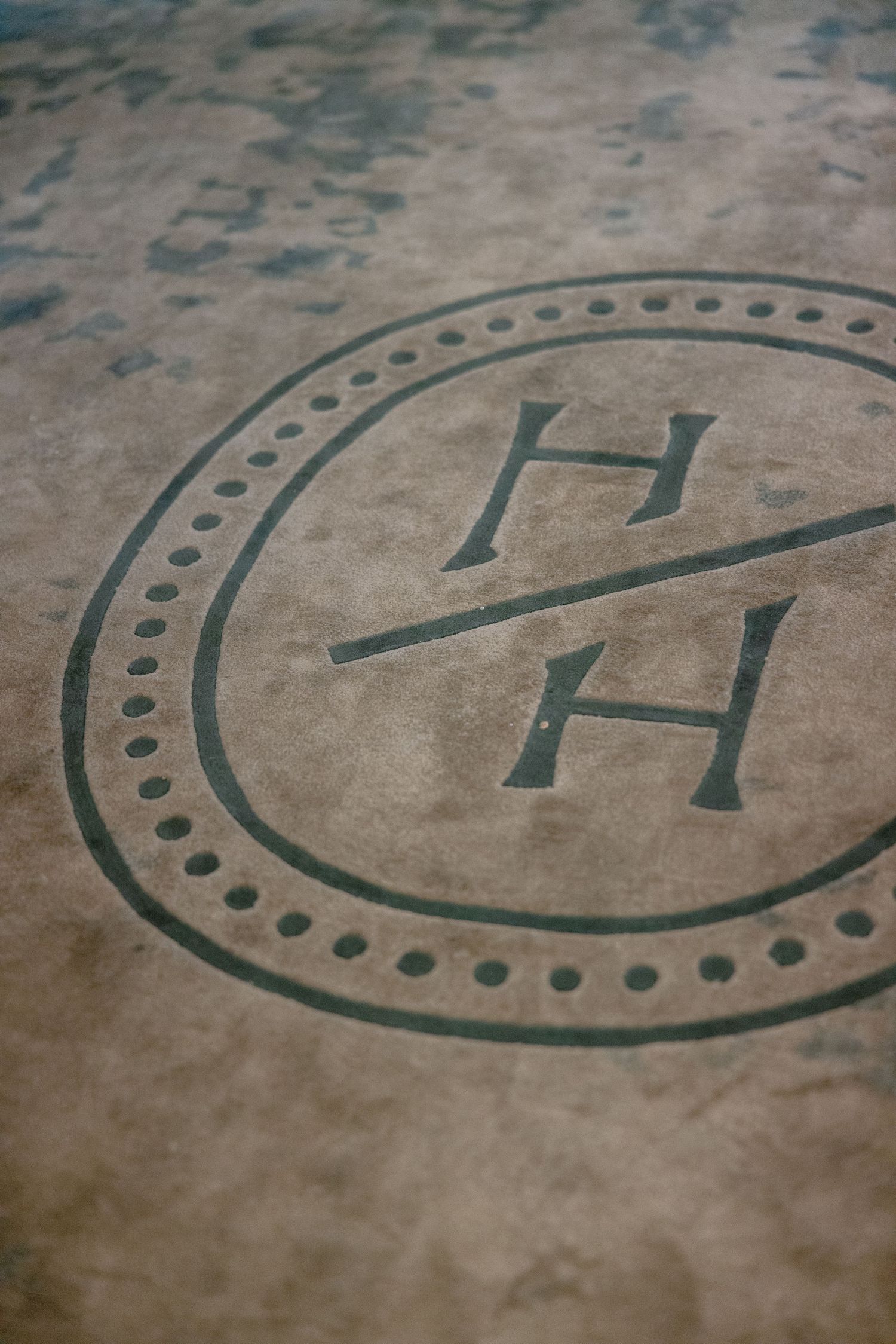 Closeup macro photo showing a decorative circular logo design with the letter H embossed on faded brown paper.