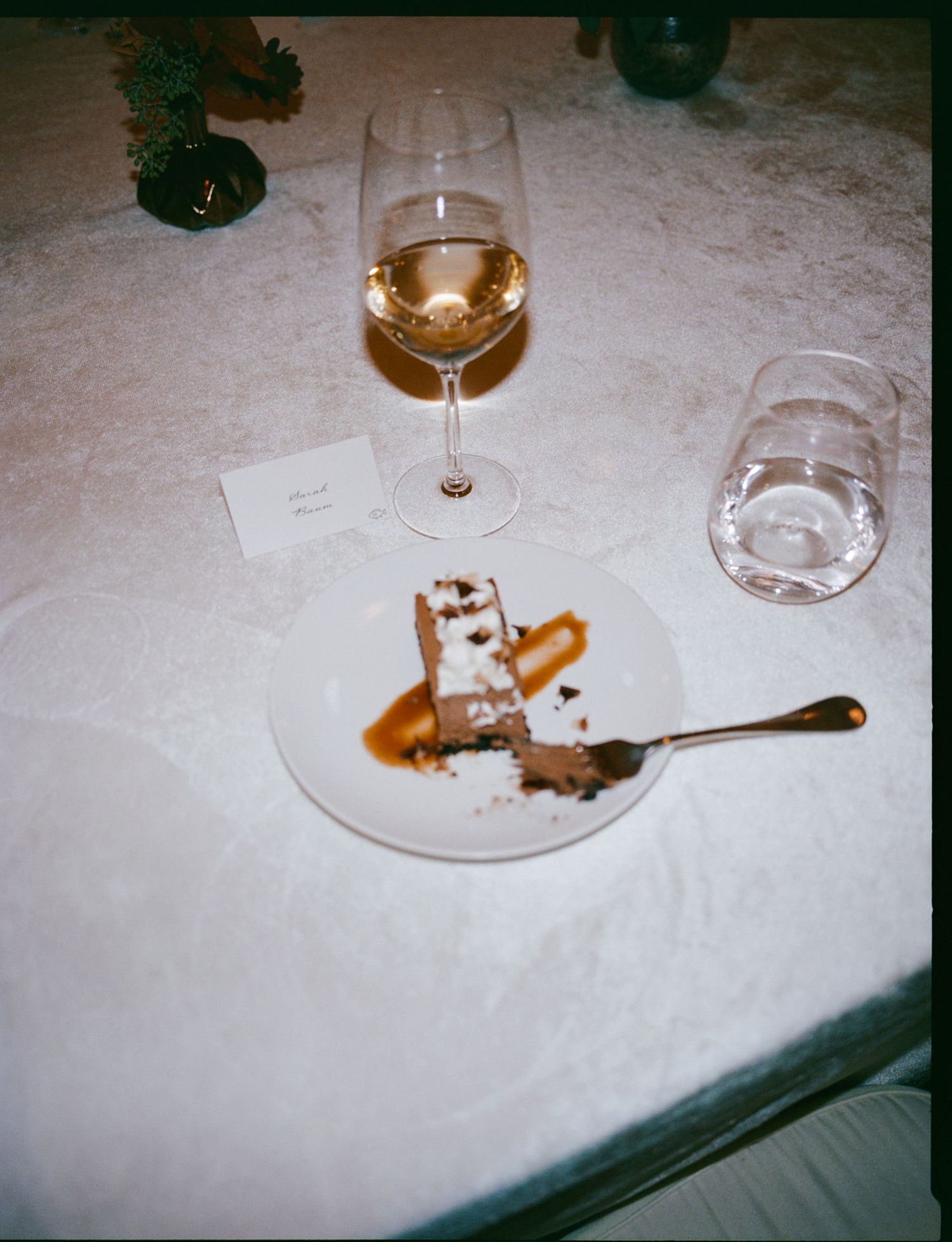 A glass of white wine and a dessert plate with chocolate cake or brownie on a white tablecloth.