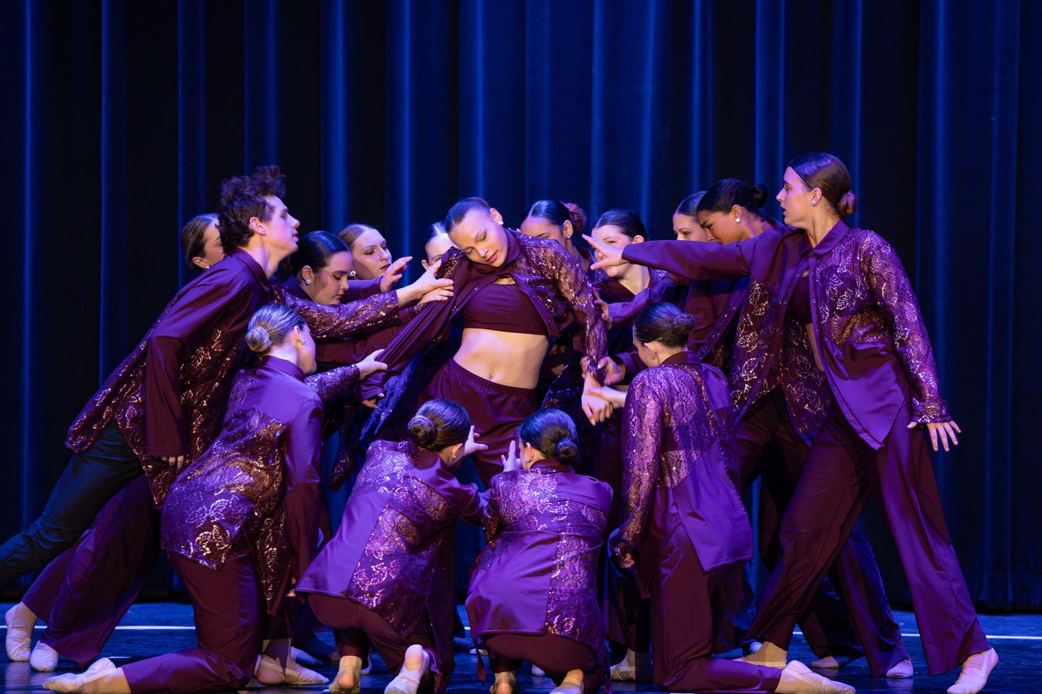 Group of dancers performing an energetic hip hop routine in purple stage lighting.