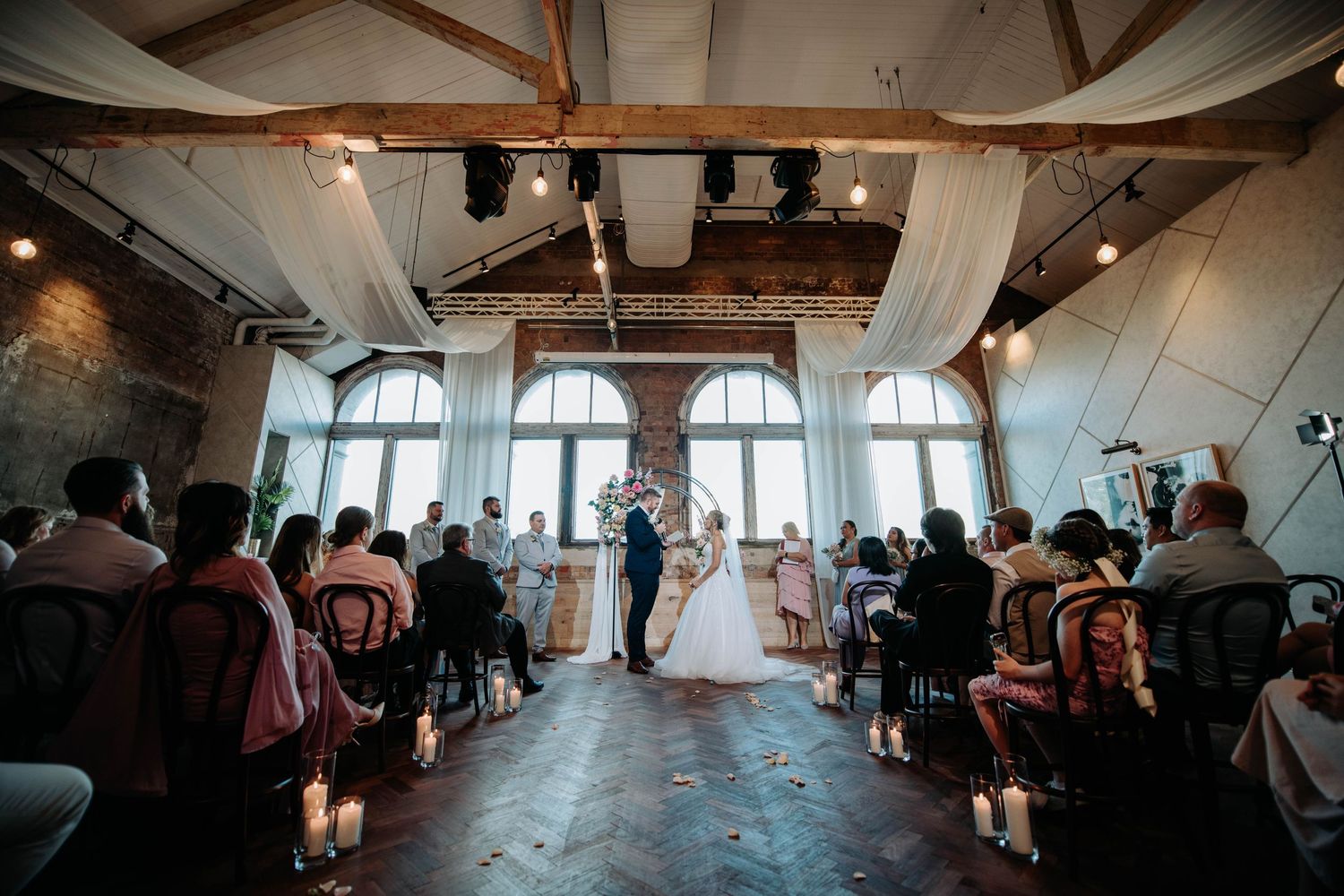 Indoor wedding ceremony at a rustic venue with wooden beams and white draping.