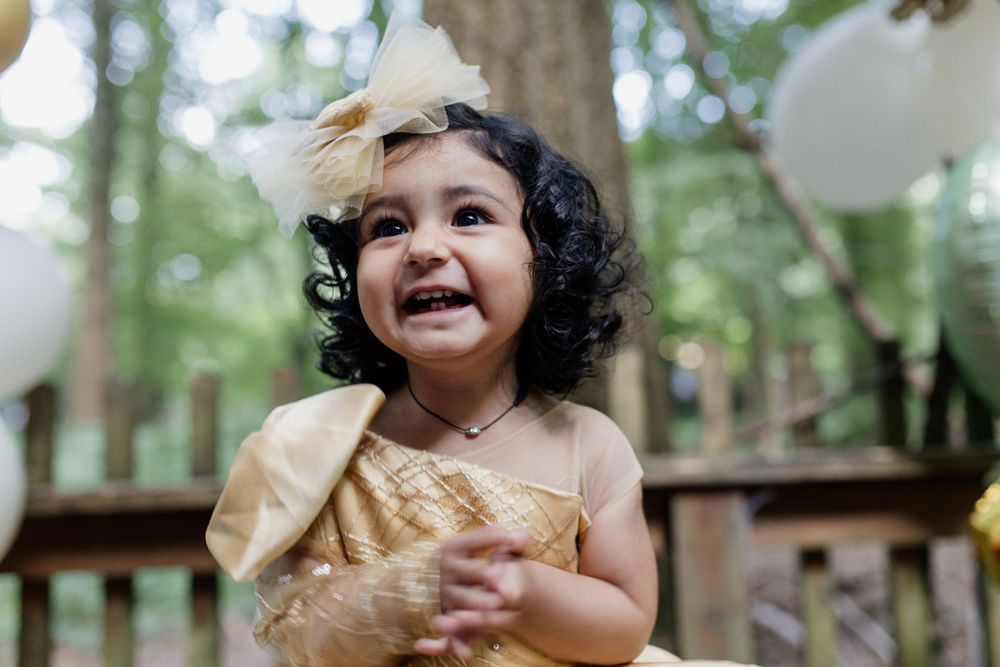 A joyful child in a yellow dress with a bow laughs during an outdoor celebration.
