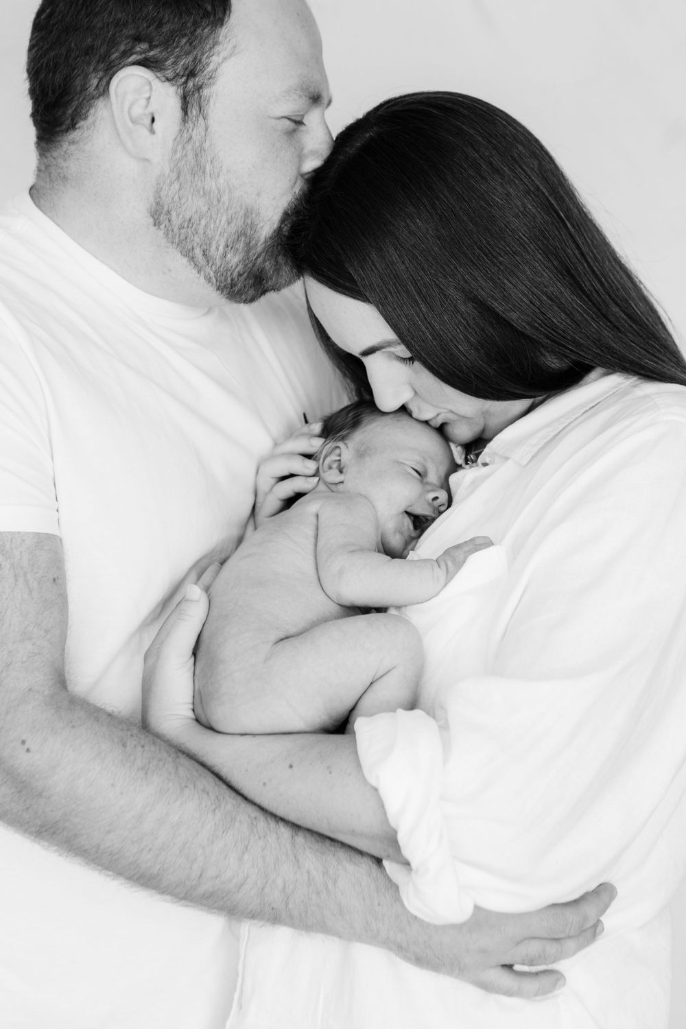 Black and white intimate newborn photography with parents holding their sleeping baby.