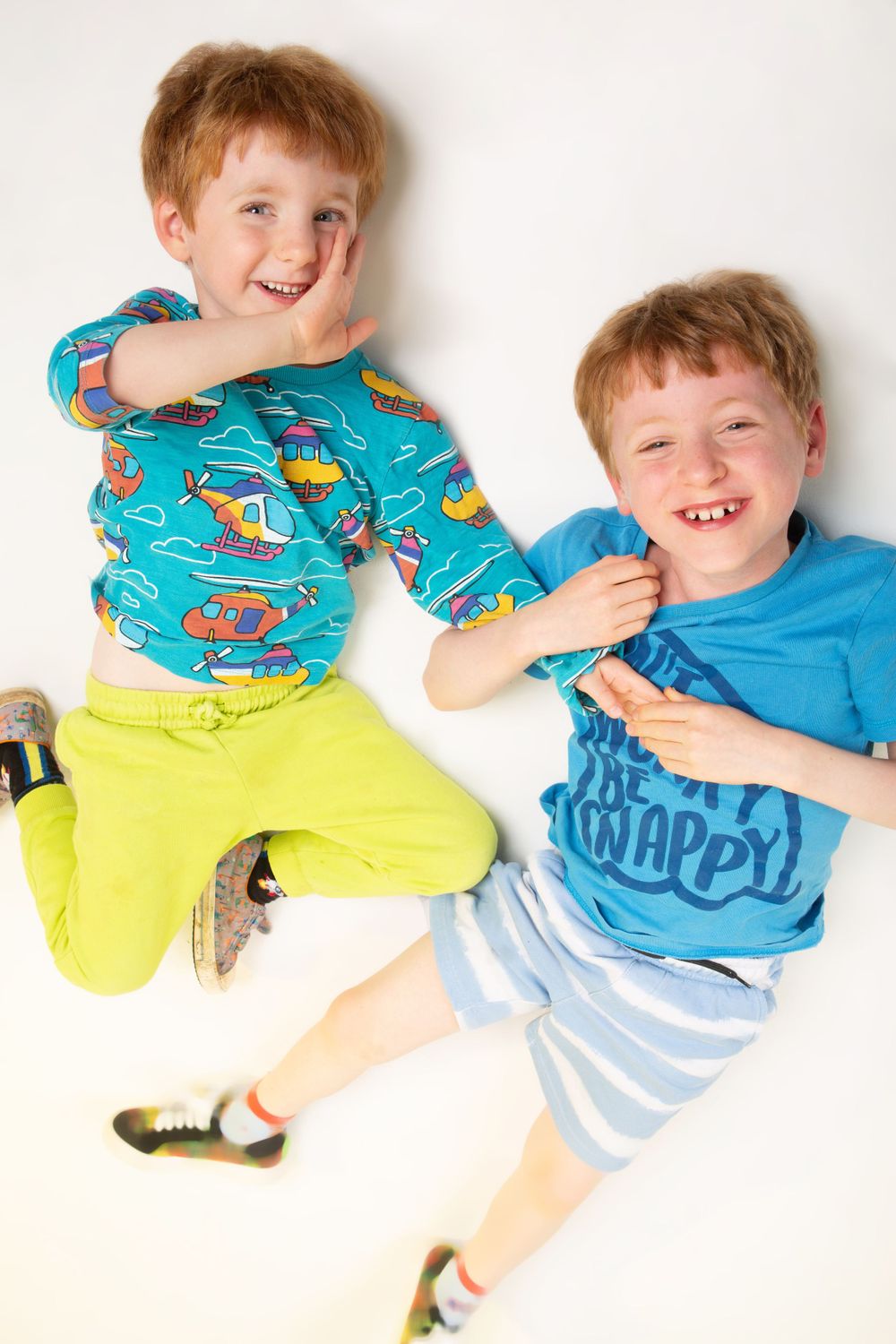 Two playful figures in bright clothing laying on white floor making silly poses.