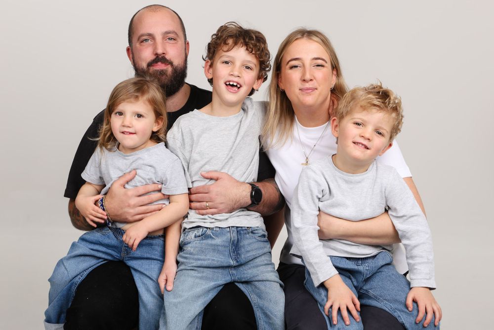 Family portrait of parents with three children sitting together wearing coordinated outfits.