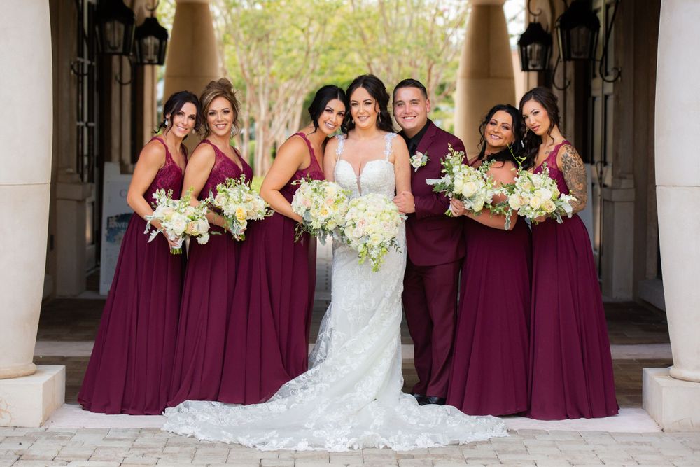 Wedding party photo of bridesmaids in burgundy dresses holding white floral bouquets.
