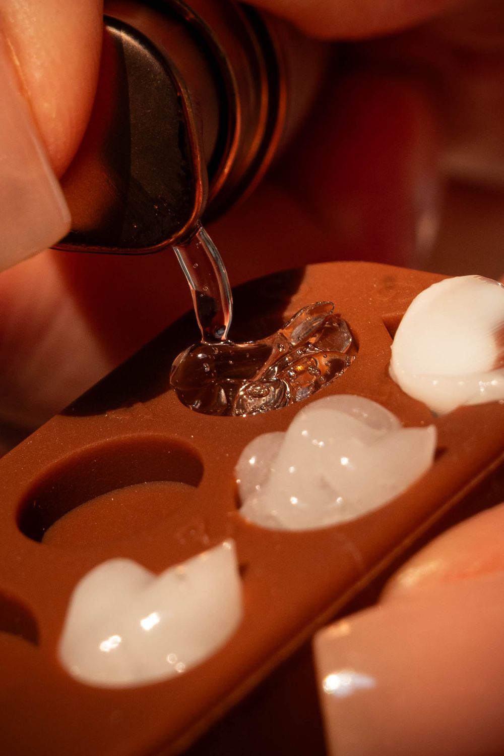 Liquid being poured into a silicone ice mold with round sphere-shaped ice balls in warm amber lighting.