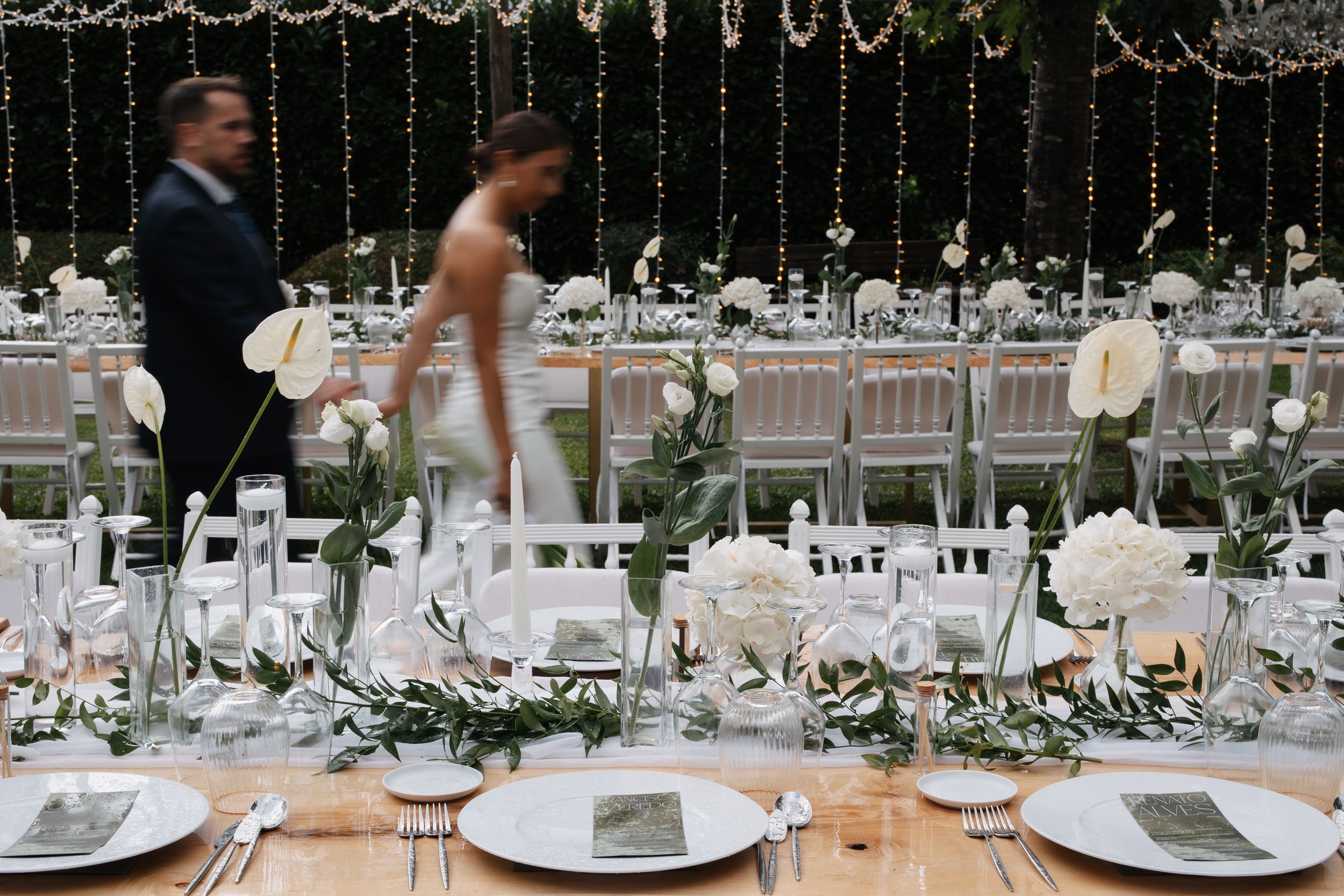 Casamento ao ar livre no Porto com decoração elegante — mesas com toalhas brancas, flores e luzes suspensas a iluminar a receção.