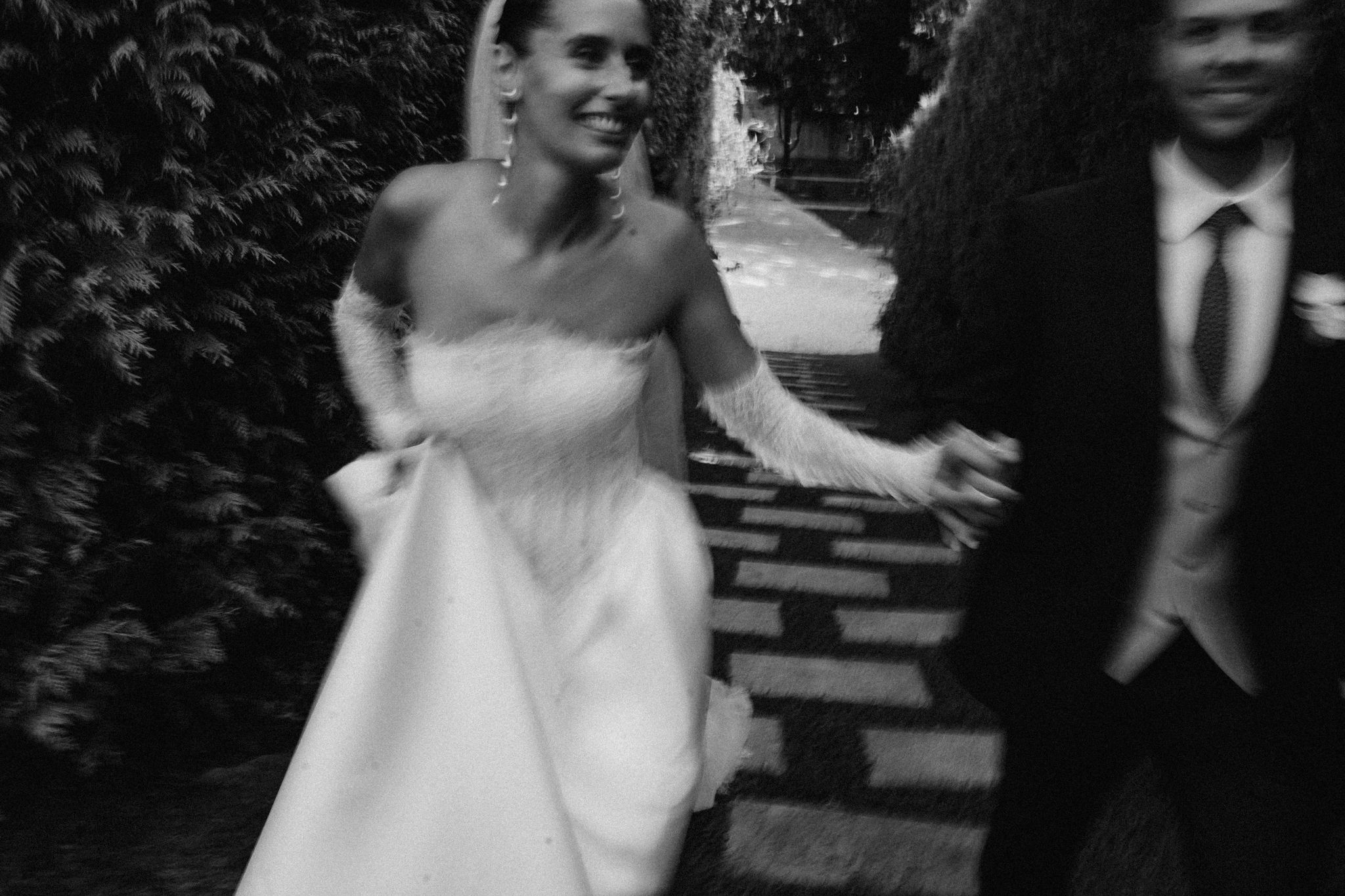 Black and white photo of a bride in a strapless gown and groom in a suit walking together outdoors.