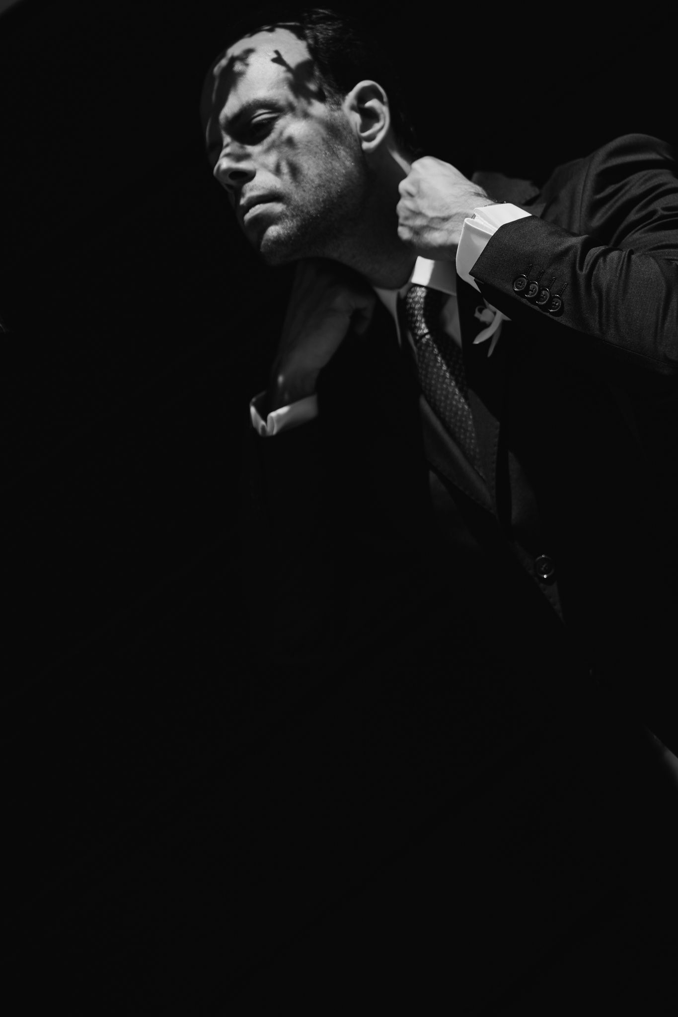Black and white noir-style photo of a bruised man in a suit being grabbed by the collar in dramatic lighting.