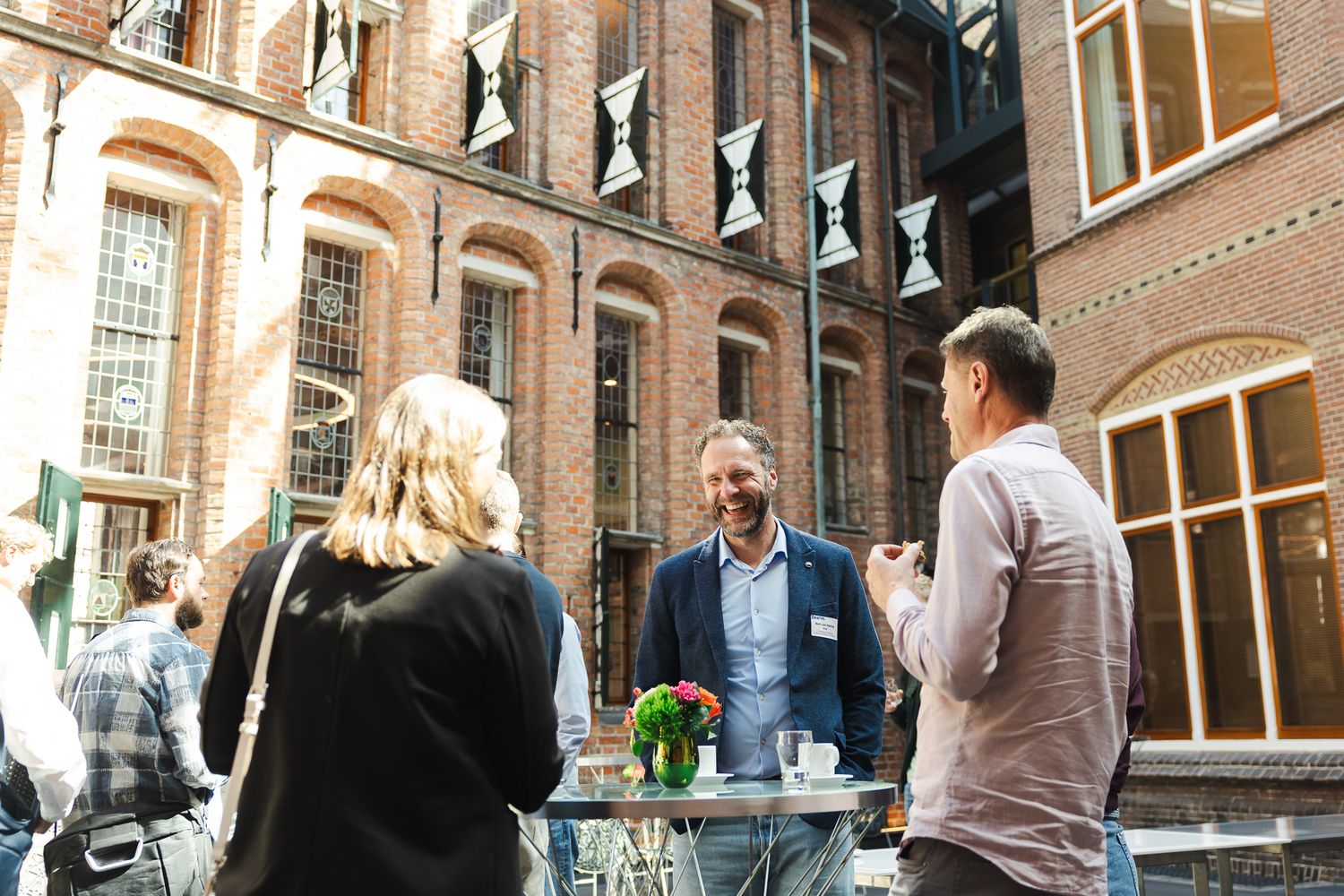 Professionals networking outdoors at a brick building courtyard, engaged in conversation around a high table.