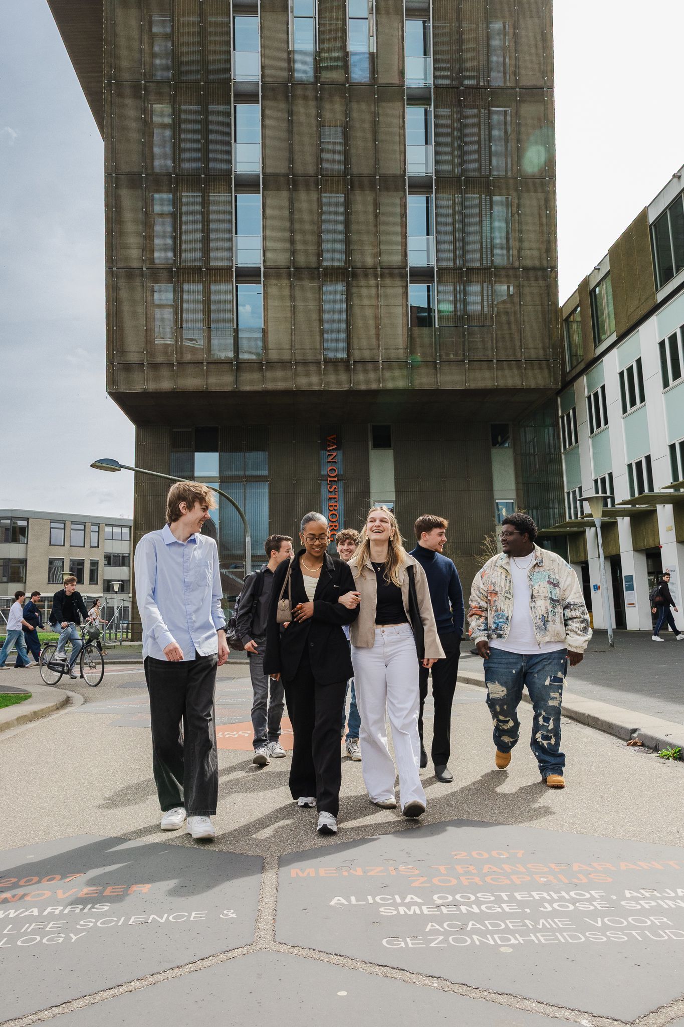 Diverse group of students walking together on a university campus with a modern brutalist building in the background.