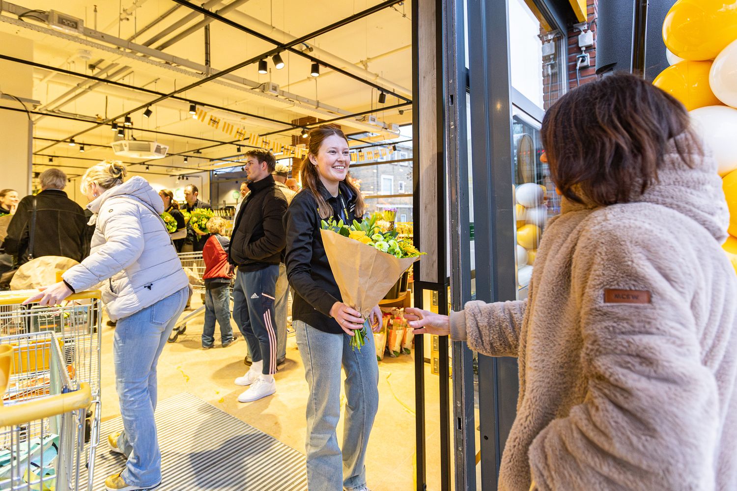 Shoppers wait in line outside a store entrance with yellow lanterns hanging from the ceiling.