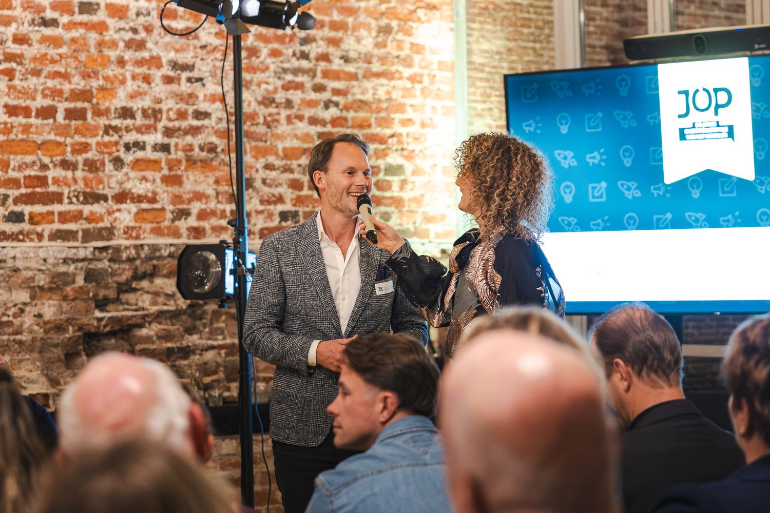 A group of people gather in a rustic brick-walled venue for a business networking or social event.
