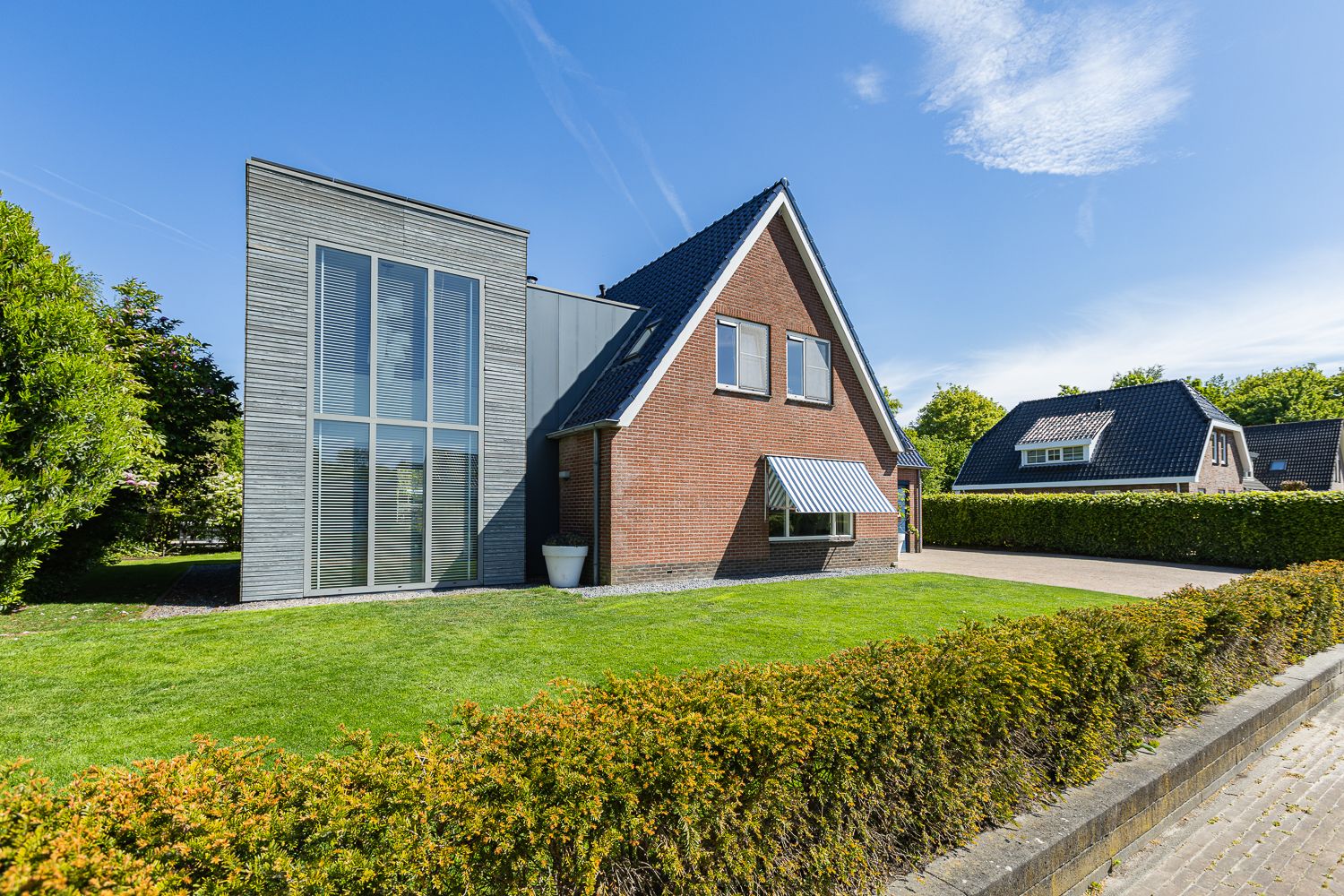 Modern architectural home with brick and metal exterior featuring large windows and manicured hedge landscaping.