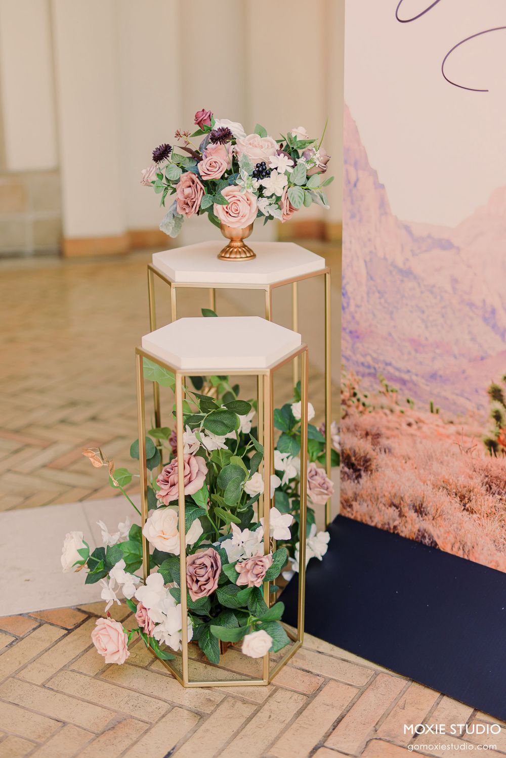 Elegant wedding table decor features hexagonal marble stands adorned with pink roses and greenery against a soft pastel backdrop.