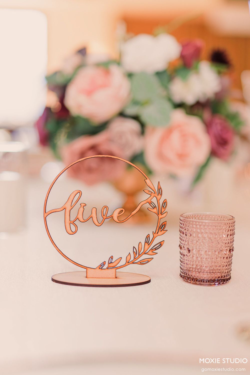 Elegant rose gold 'love' script wedding table decor with blush floral arrangements and textured glass votives.