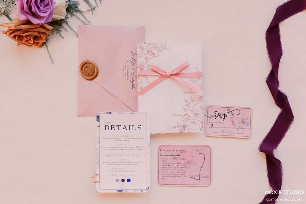 Pink and white wedding invitation suite with floral details and a burgundy ribbon accent.