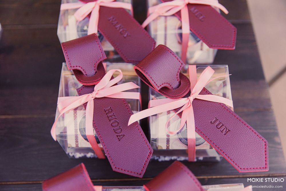 Pink leather luggage tags with bows arranged in a row on a dark wooden surface.